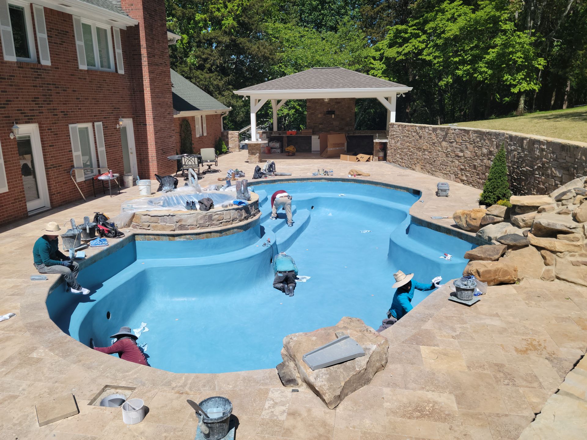 A large blue swimming pool is being painted in front of a brick house.