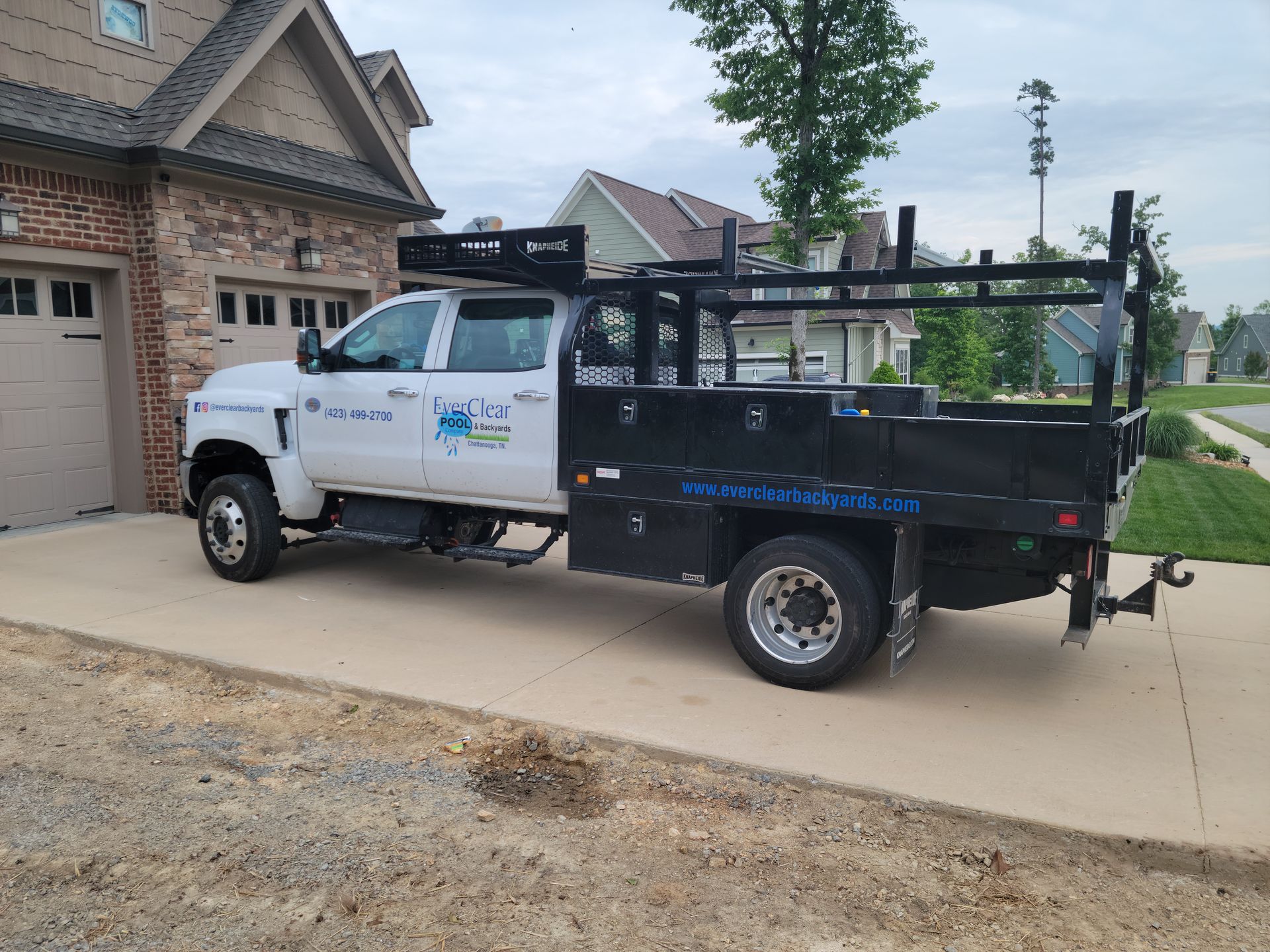 A white truck with a black bed is parked in front of a house.