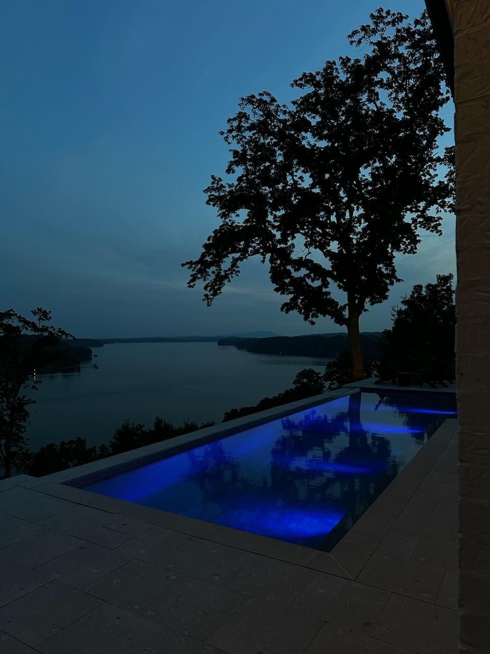 A swimming pool lit up with blue lights overlooking a body of water