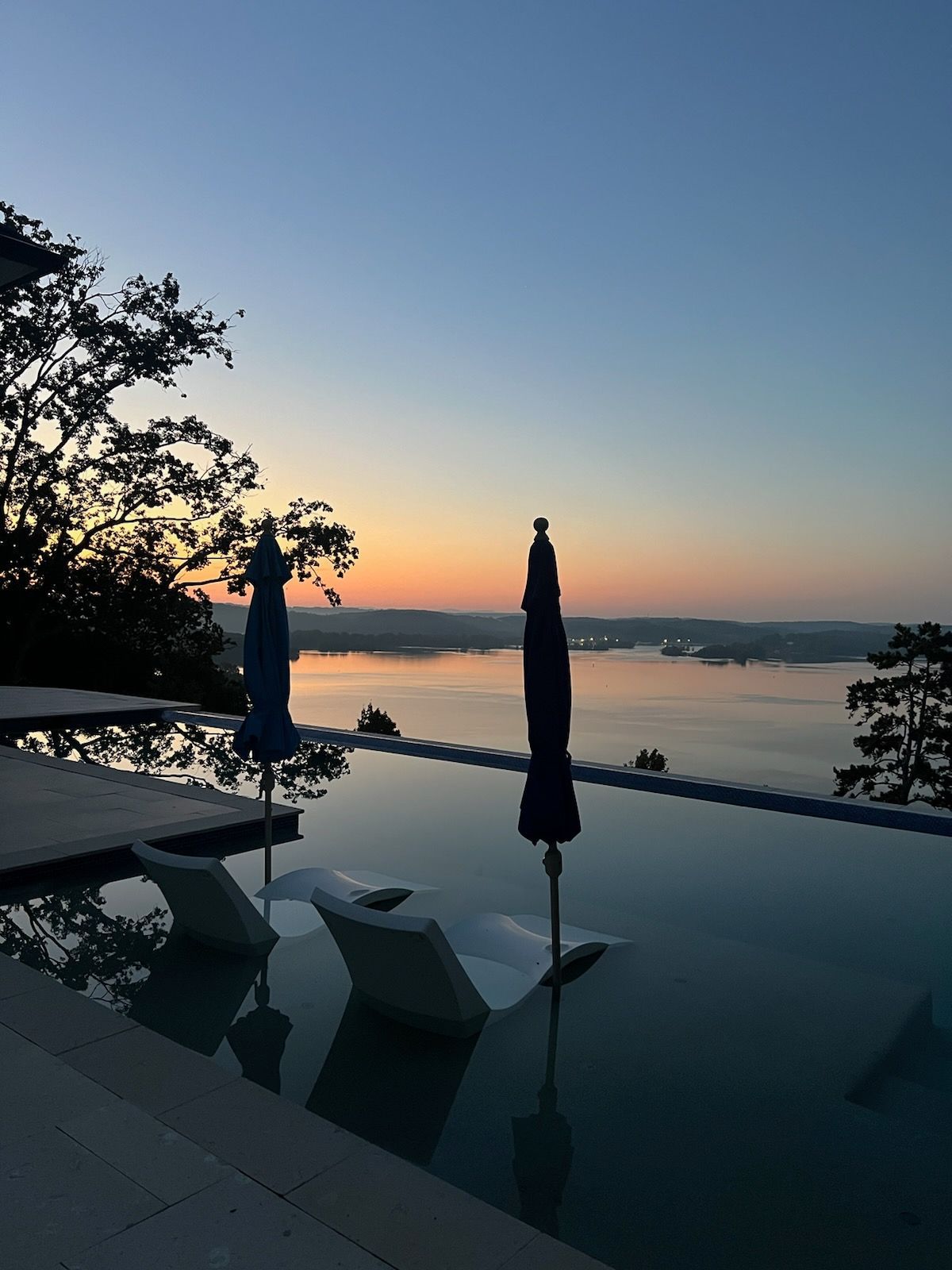An infinity pool with chairs and umbrellas overlooking a body of water at sunset