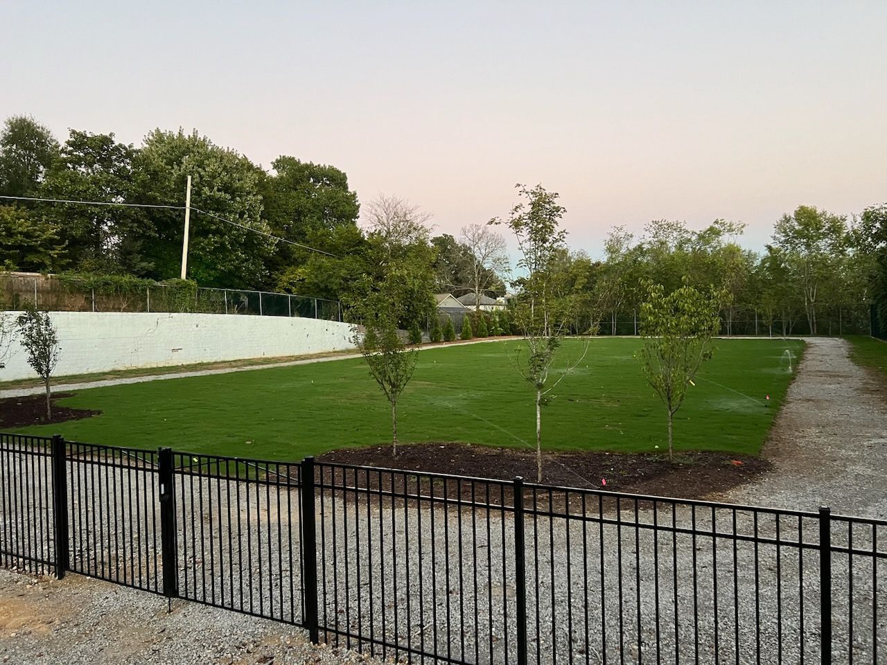 A fence surrounds a grassy field with trees in the background.