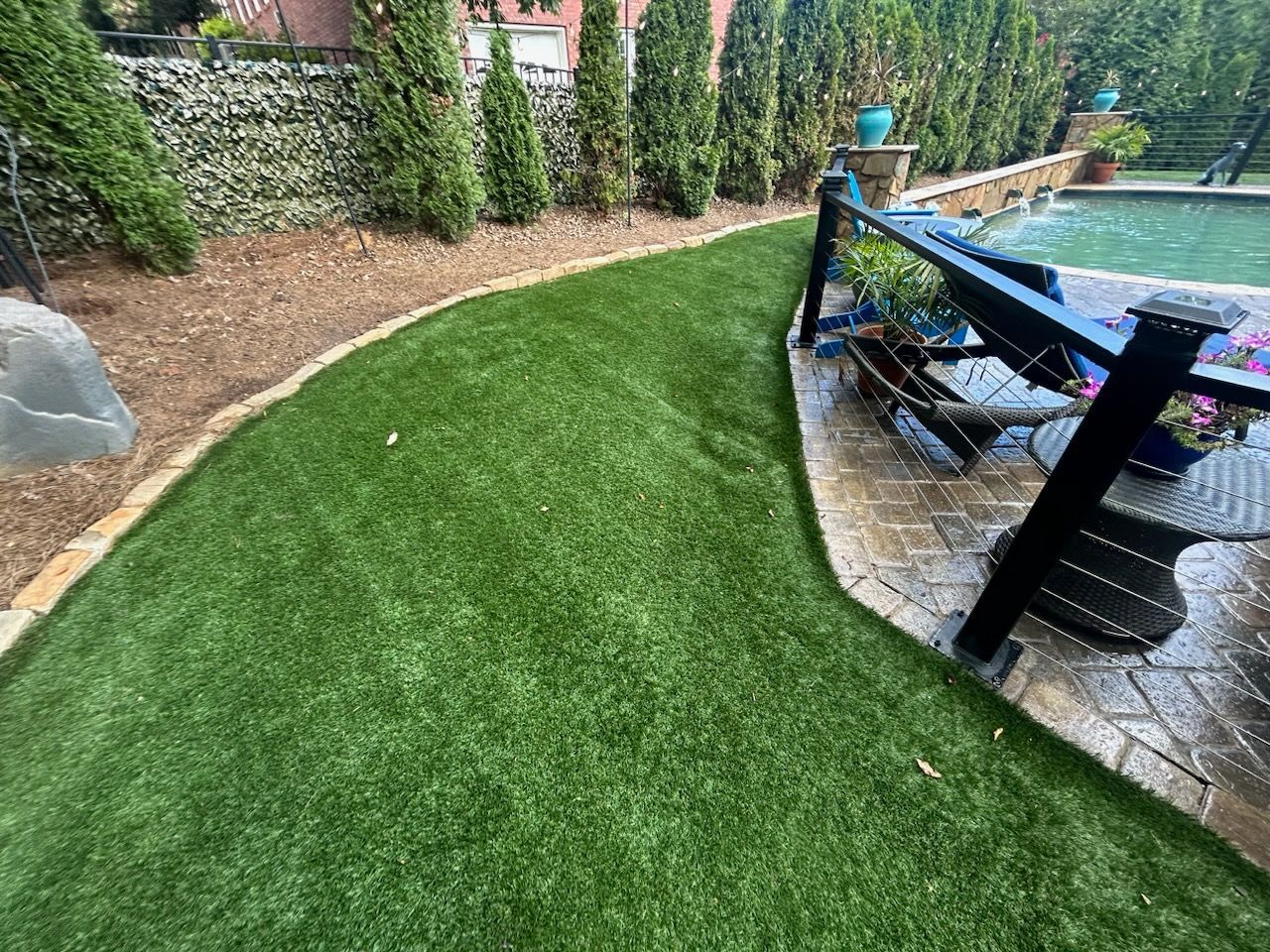 A lush green lawn next to a swimming pool in a backyard.