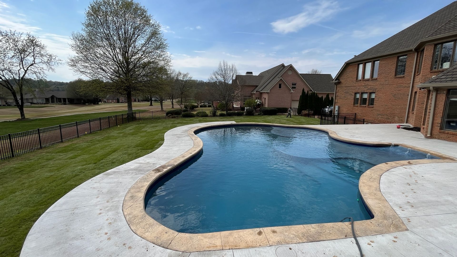 A large swimming pool is in the backyard of a brick house.