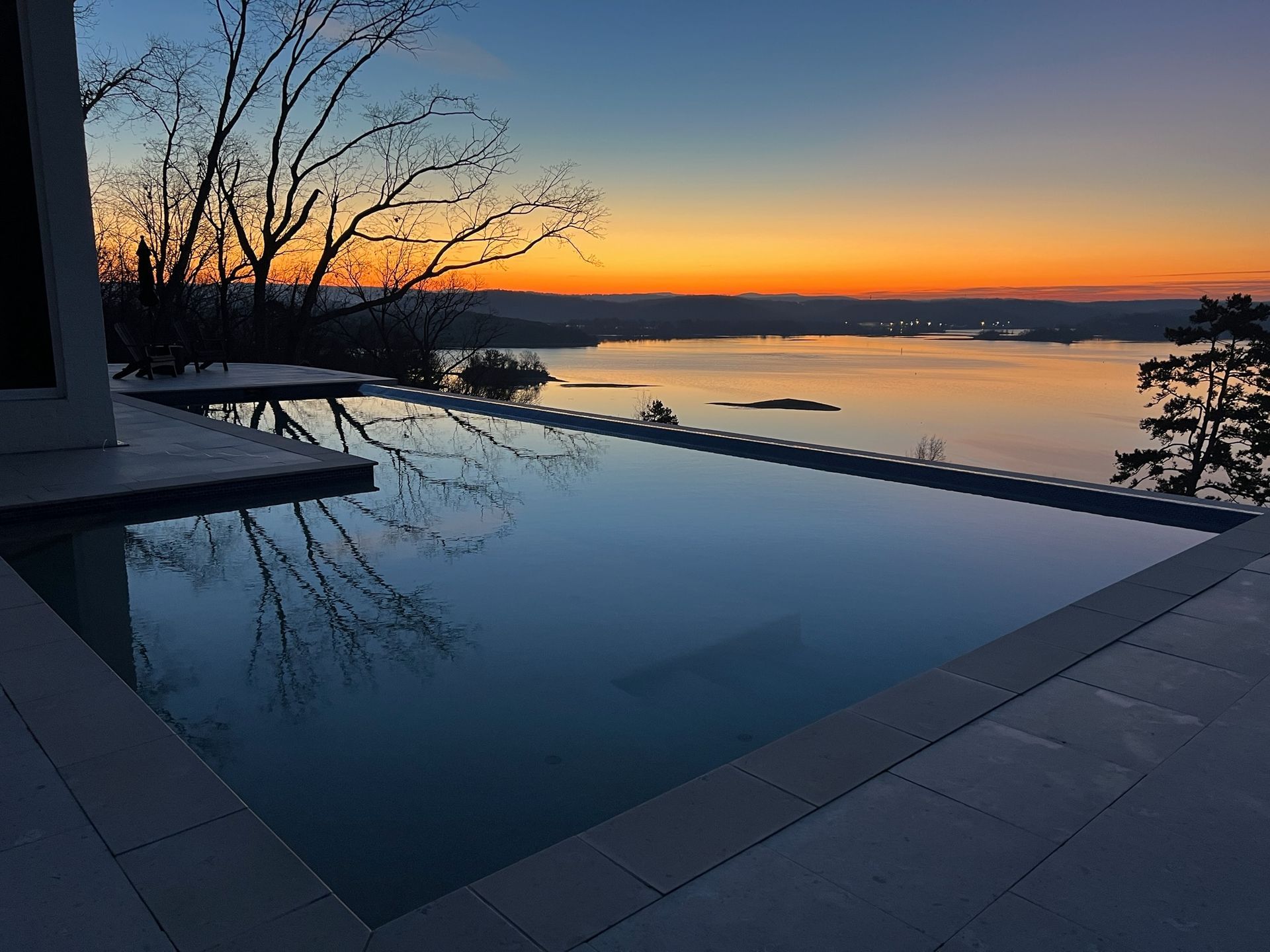An infinity pool with a view of a lake at sunset.