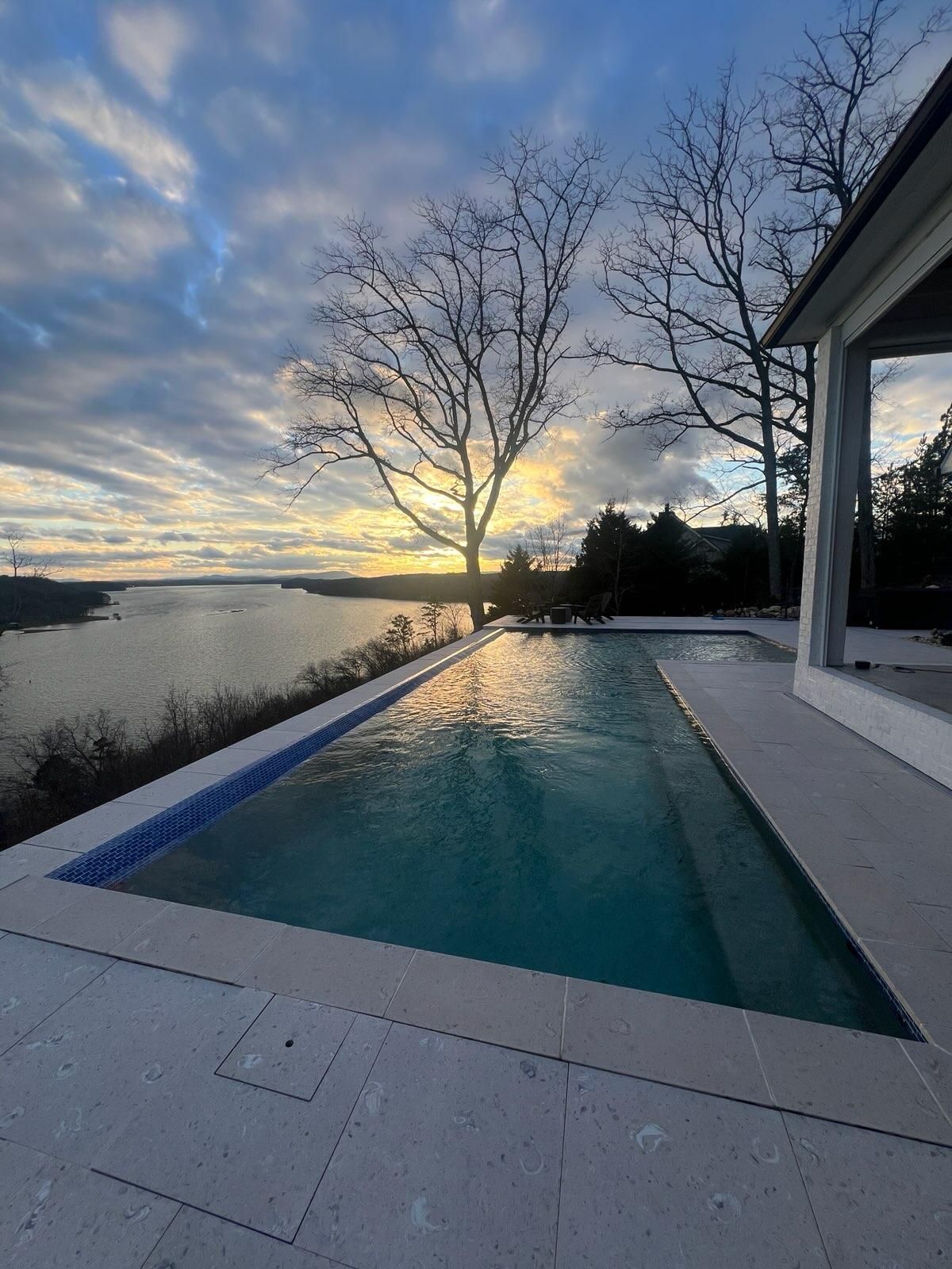 A large swimming pool with a view of a lake at sunset.