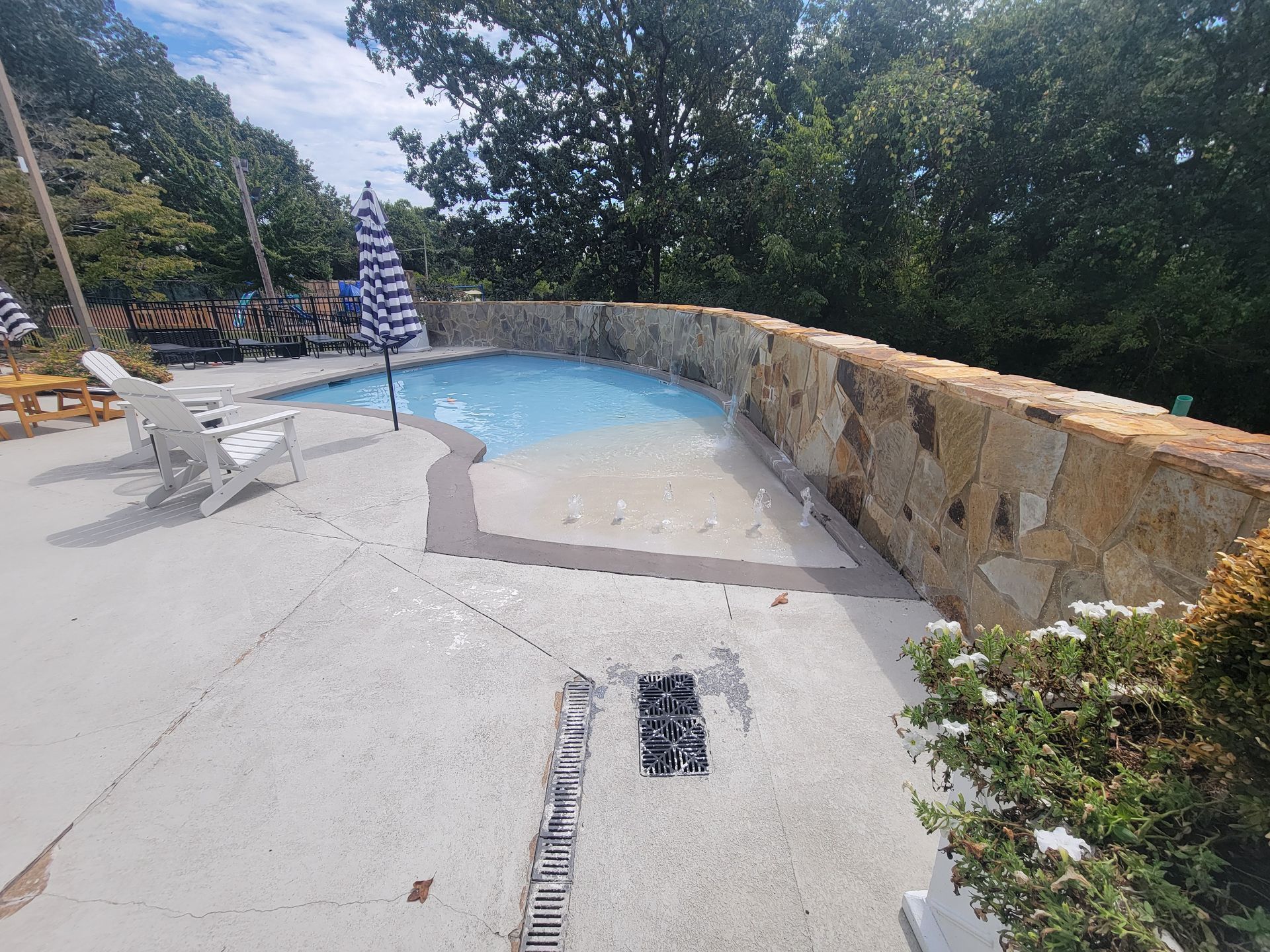 A large swimming pool is surrounded by a stone wall and chairs.