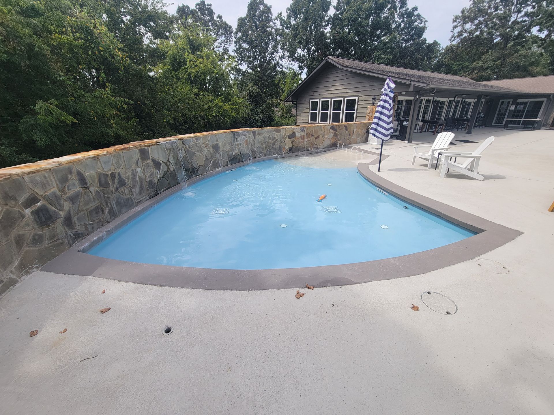 A large swimming pool is surrounded by a stone wall and chairs.