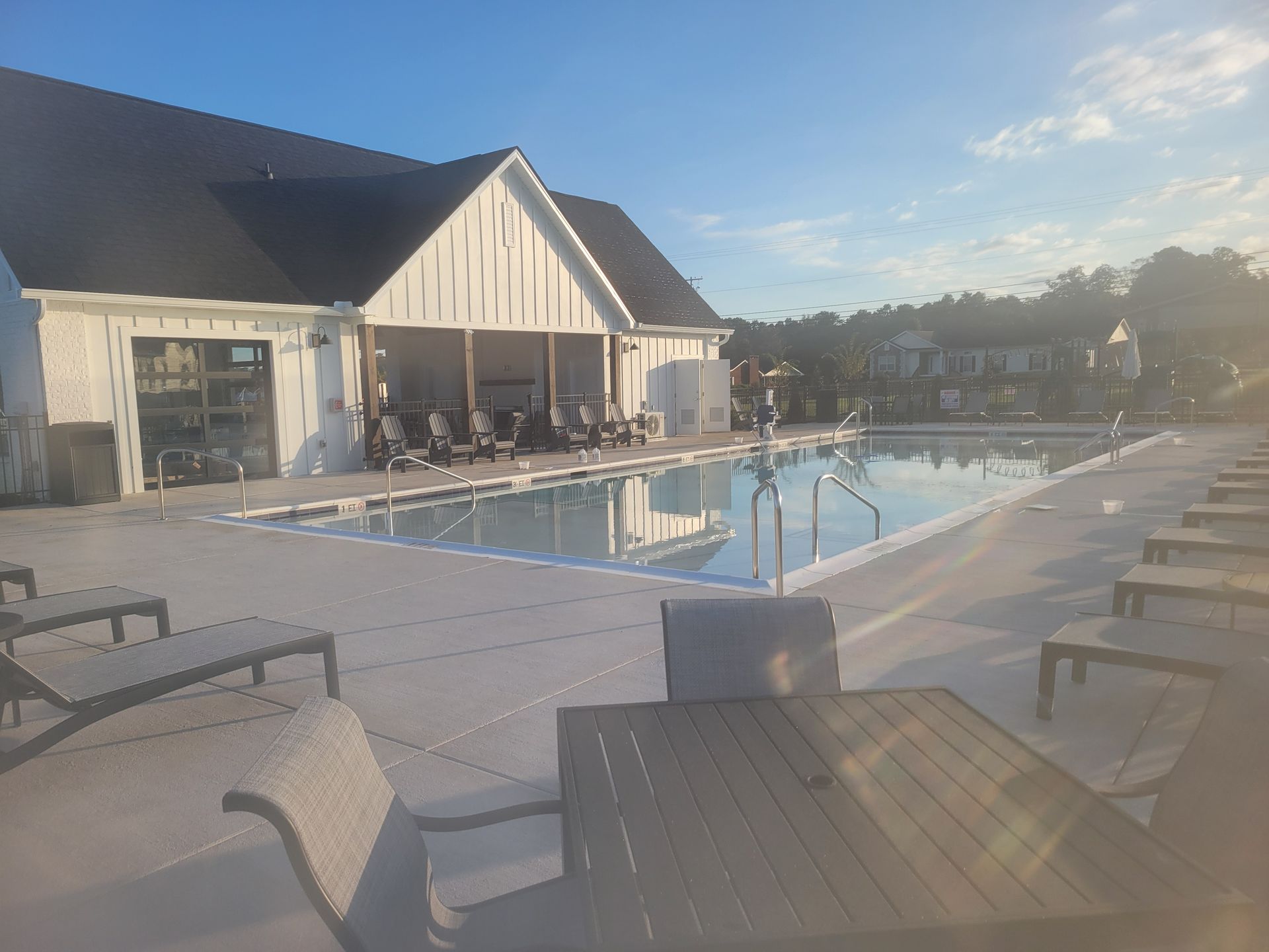 A large swimming pool surrounded by chairs and tables in front of a building.