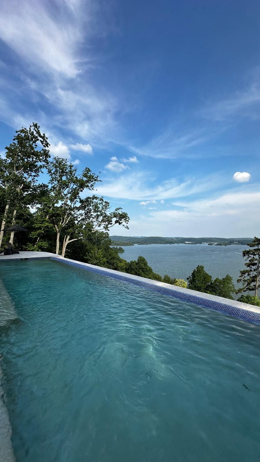 An infinity pool with a view of a lake on a sunny day.
