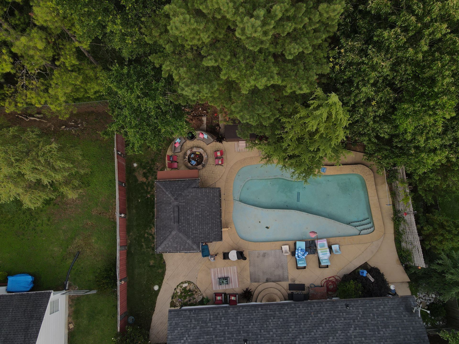 An aerial view of a backyard with a swimming pool surrounded by trees.