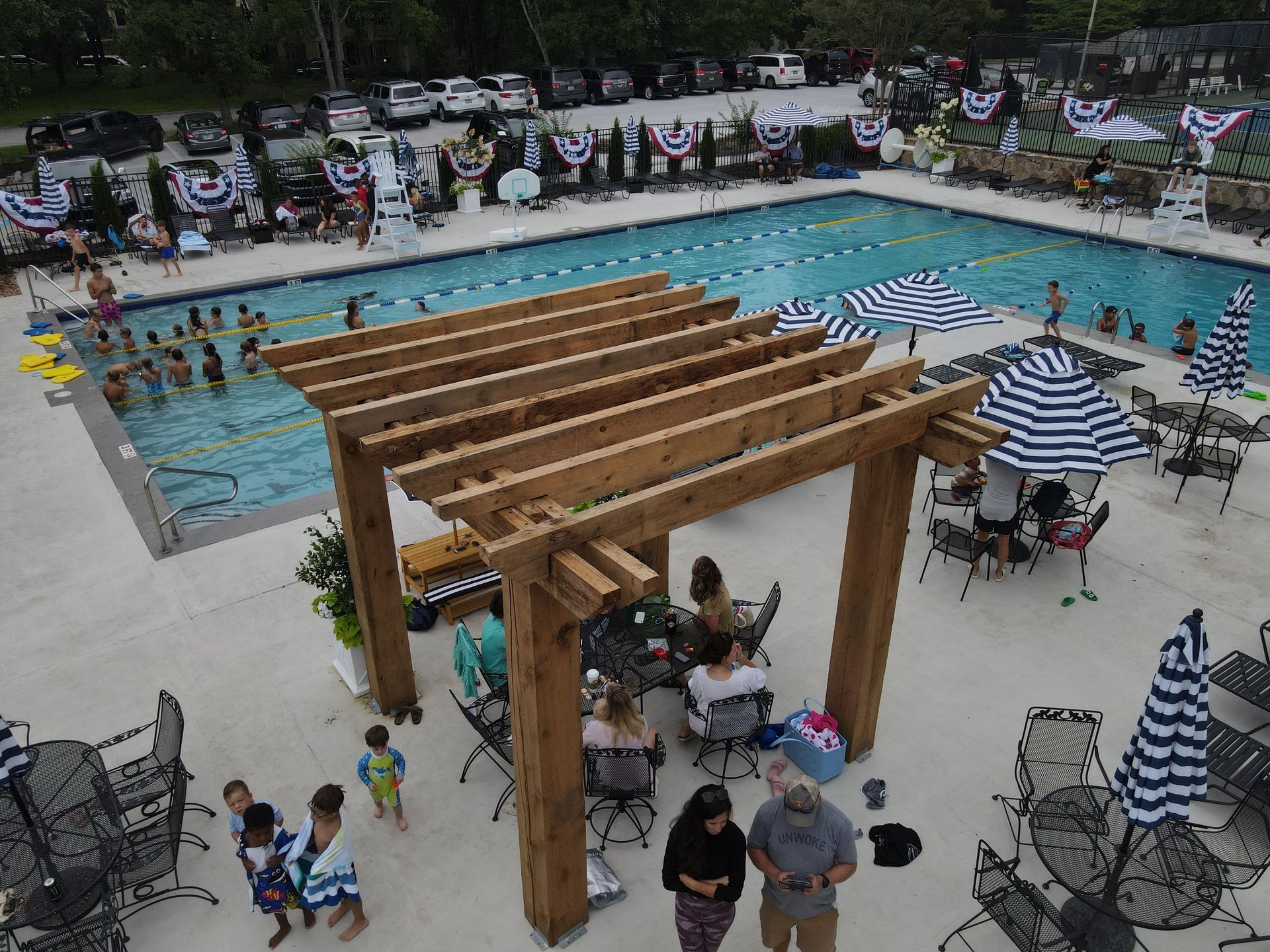 A group of people are sitting under a pergola near a swimming pool.