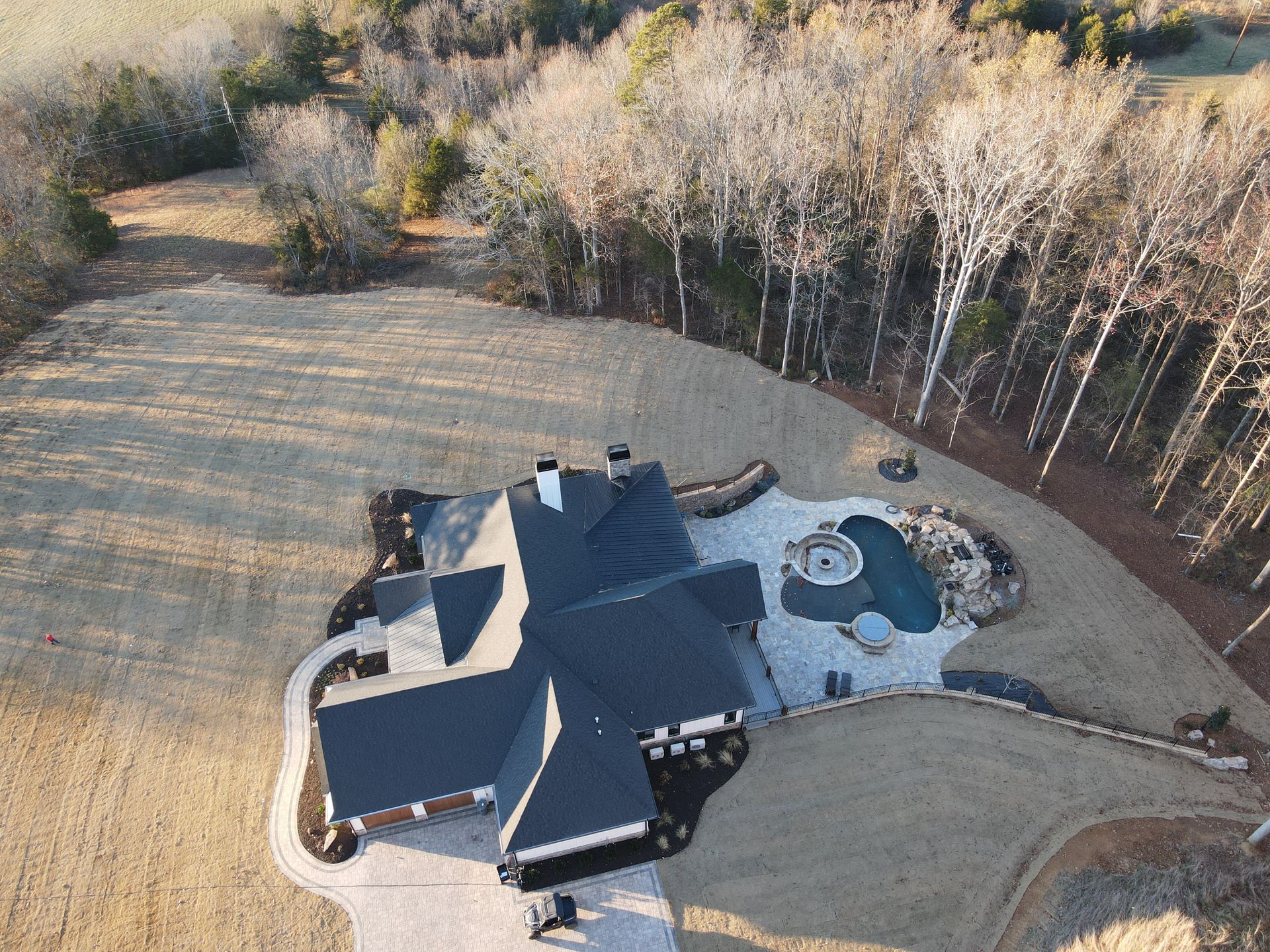 An aerial view of a house with a pool in the backyard surrounded by trees.