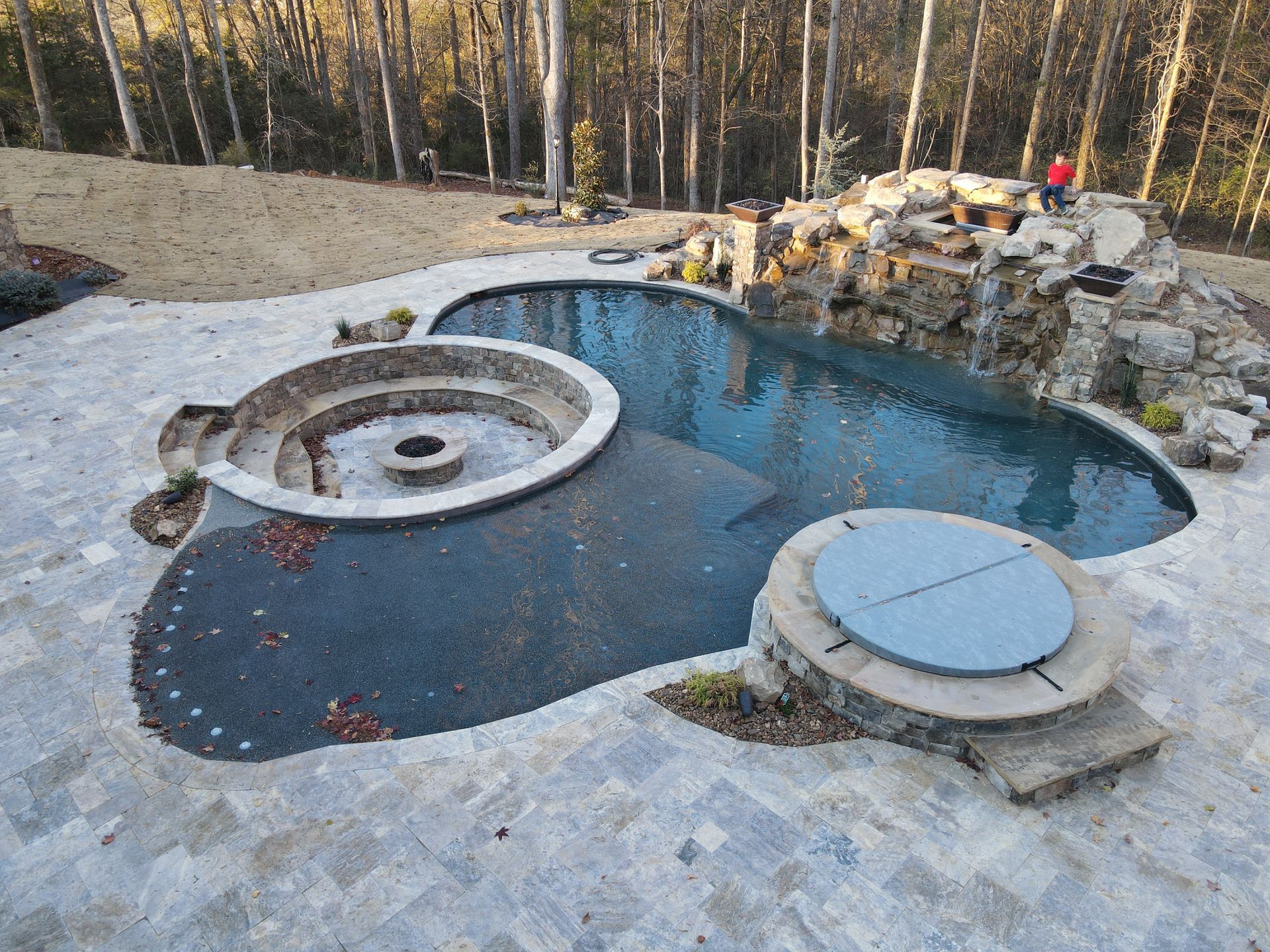 A large swimming pool with a fire pit in the middle surrounded by trees.