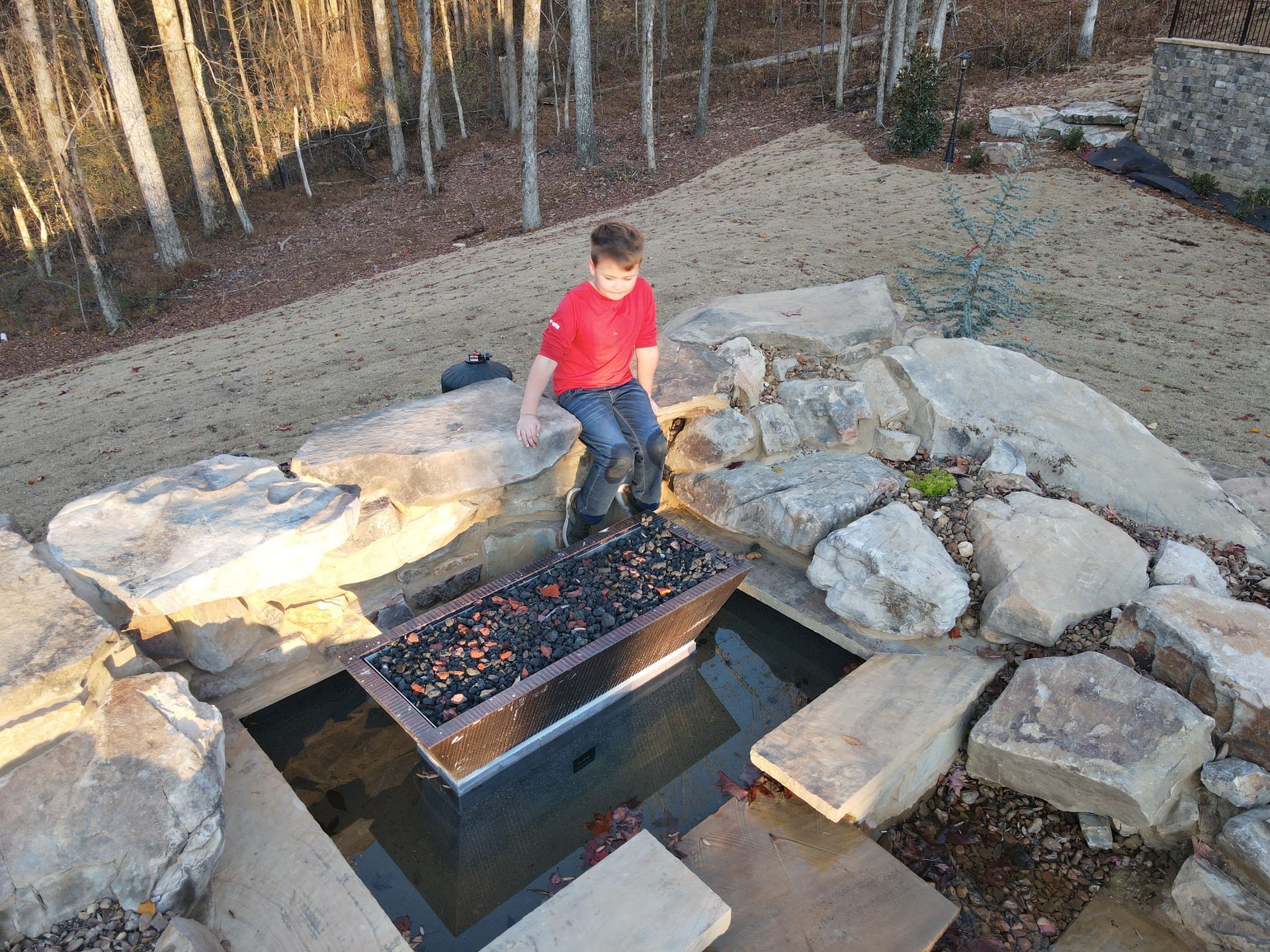 A young boy is sitting on a rock next to a fire pit.