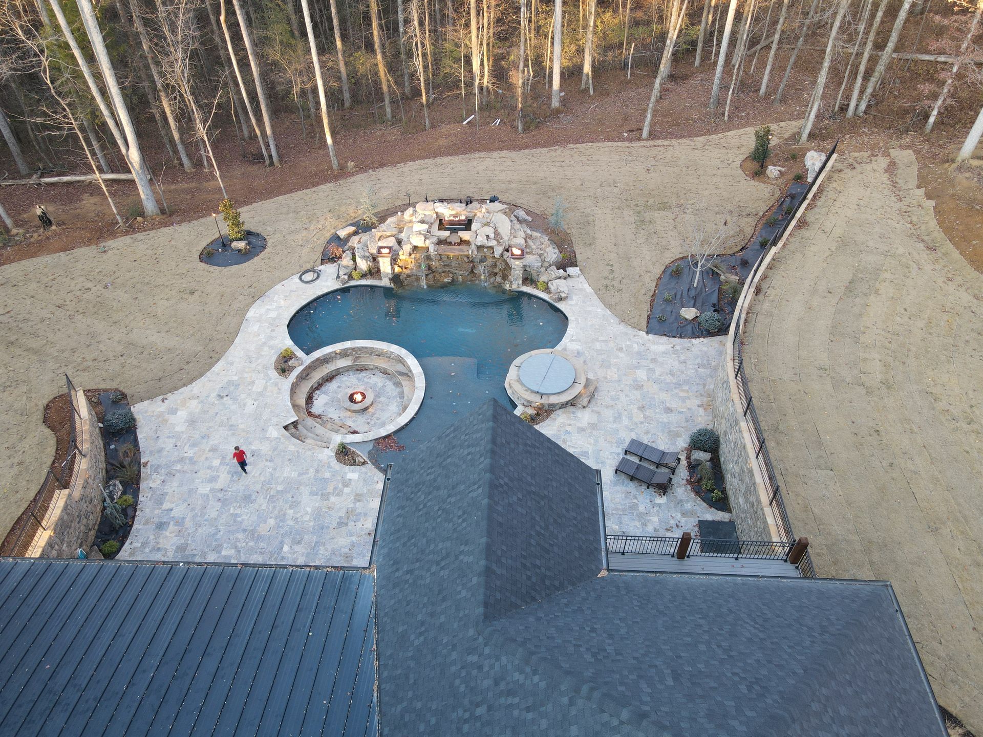 An aerial view of a house with a large pool in the backyard surrounded by trees.