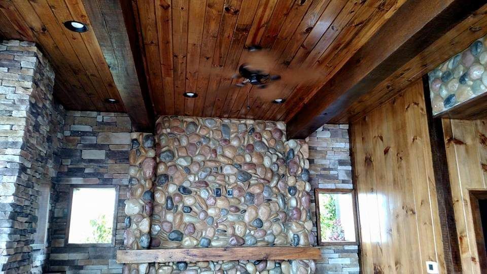 A living room with a stone fireplace and wooden ceiling.
