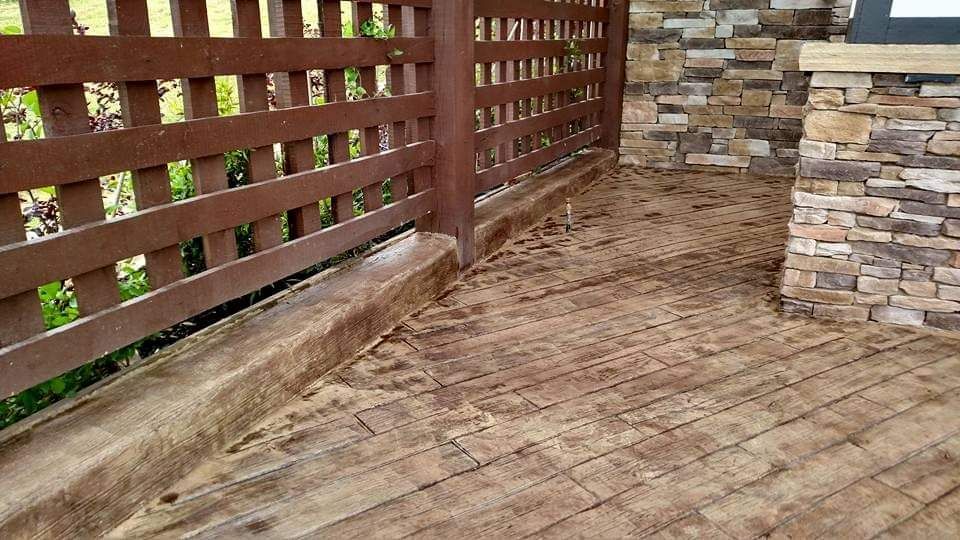 A wooden fence surrounds a brick walkway next to a stone wall.