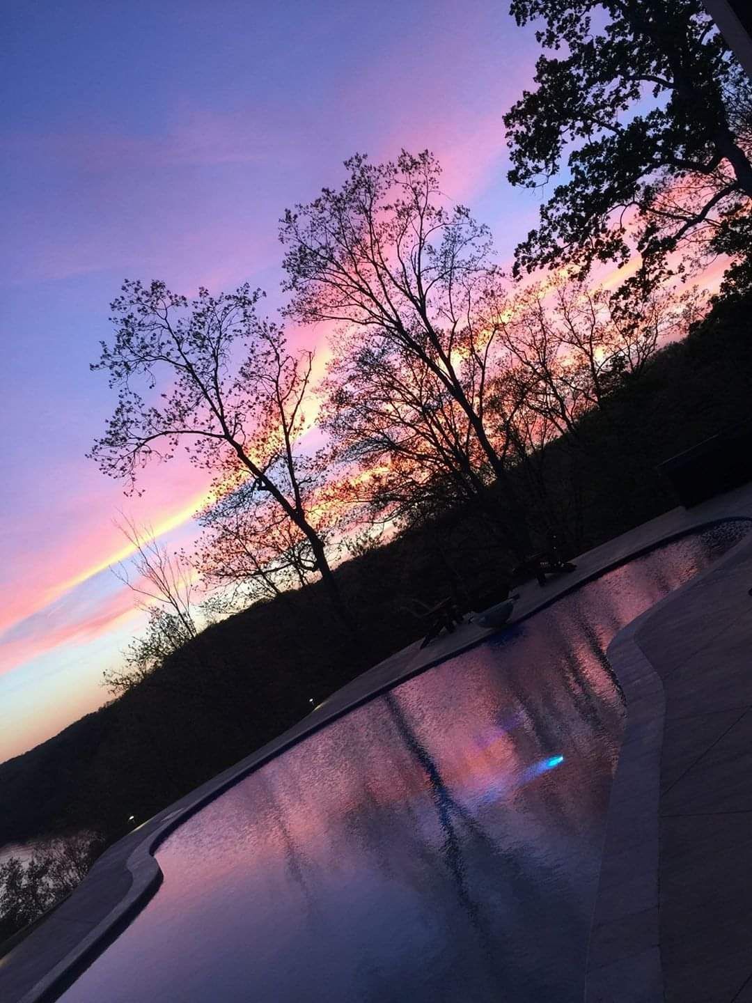 A sunset over a swimming pool with trees in the background