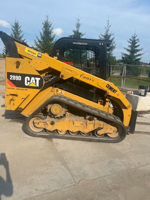 A yellow cat skid steer is parked on the side of the road