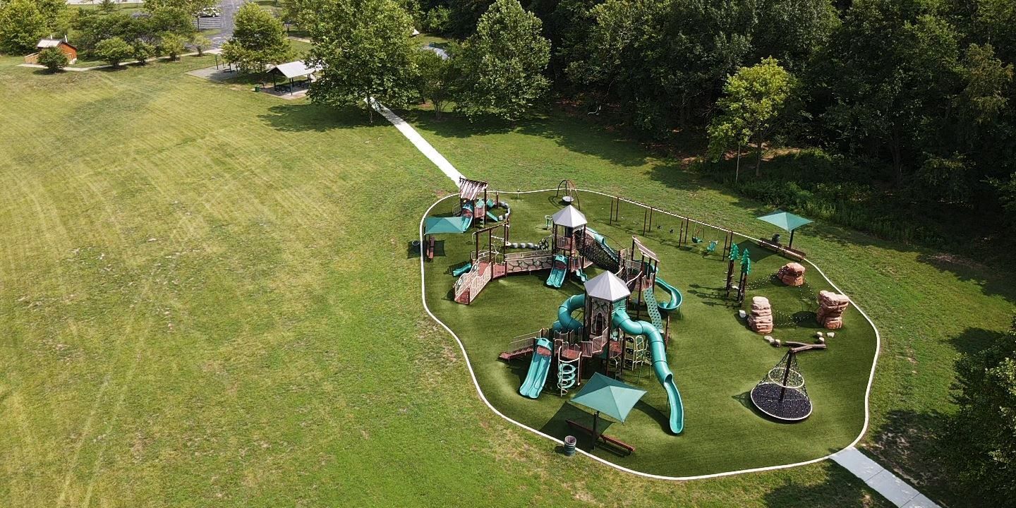 An aerial view of a playground in a park surrounded by trees.