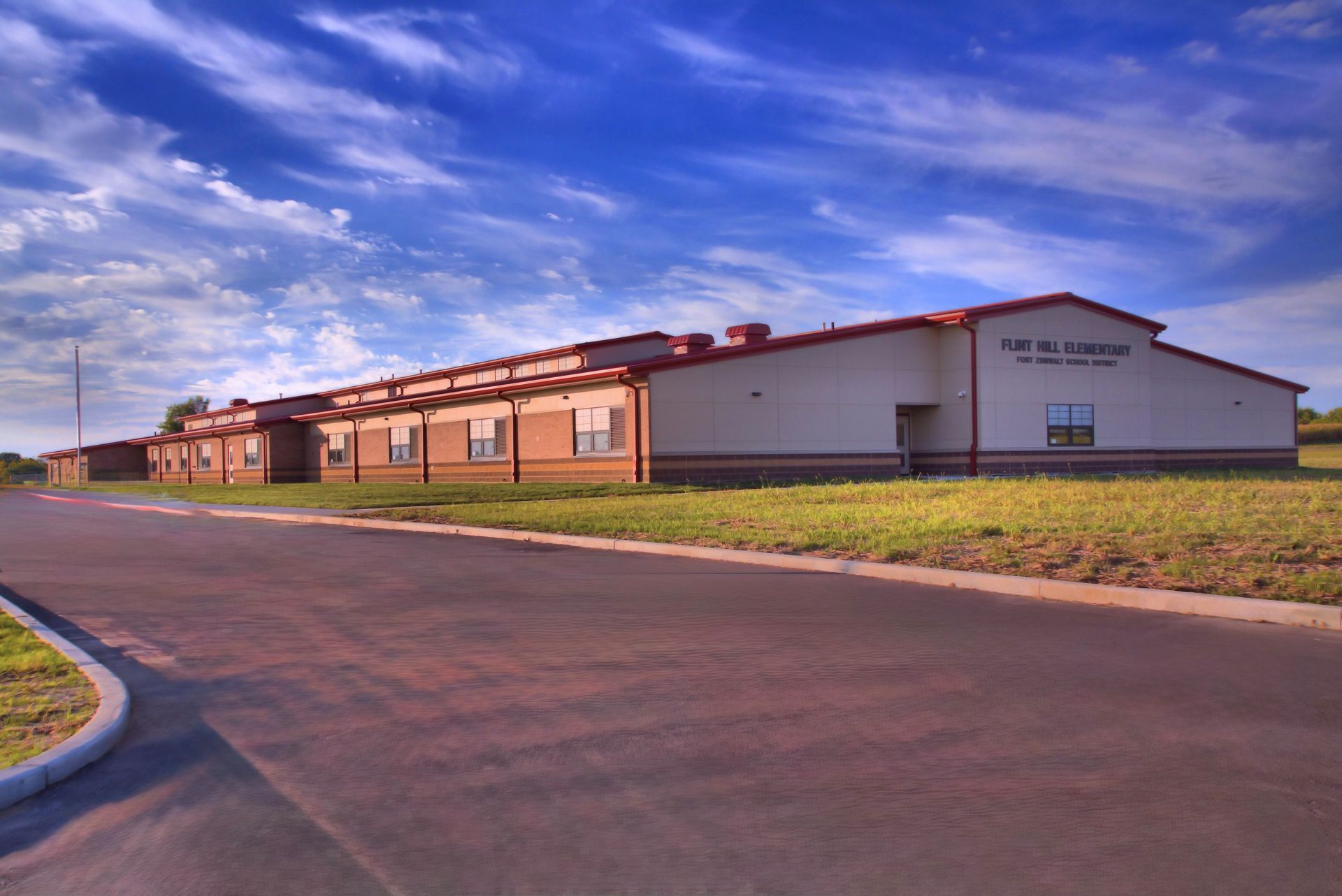 A large white building with a red roof is sitting in the middle of a grassy field.