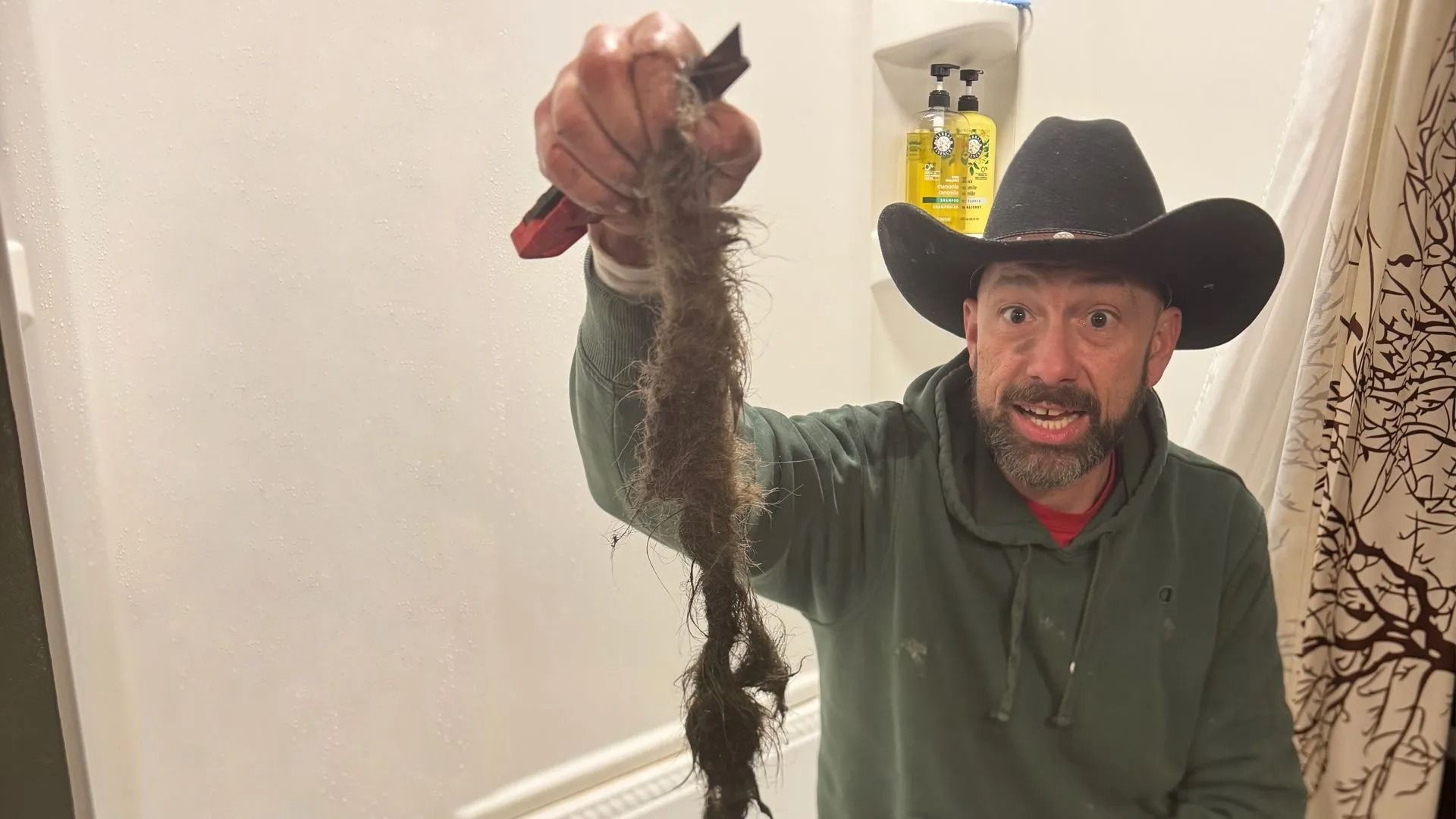 Man in a black cowboy hat holding up a long, muddy root indoors