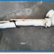 White painted pipe lying on concrete floor, secured with a black zip tie and connected to a flange end