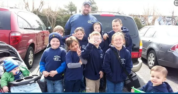 Group of people in blue shirts posing outdoors in front of parked vehicles, smiling.