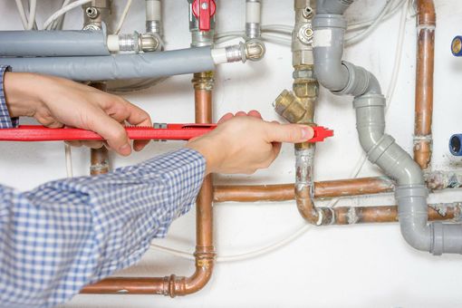 Plumber tightening pipes under a sink with a red wrench in a utility area