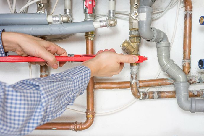 Plumber tightening pipes under a sink with a red wrench in a utility area