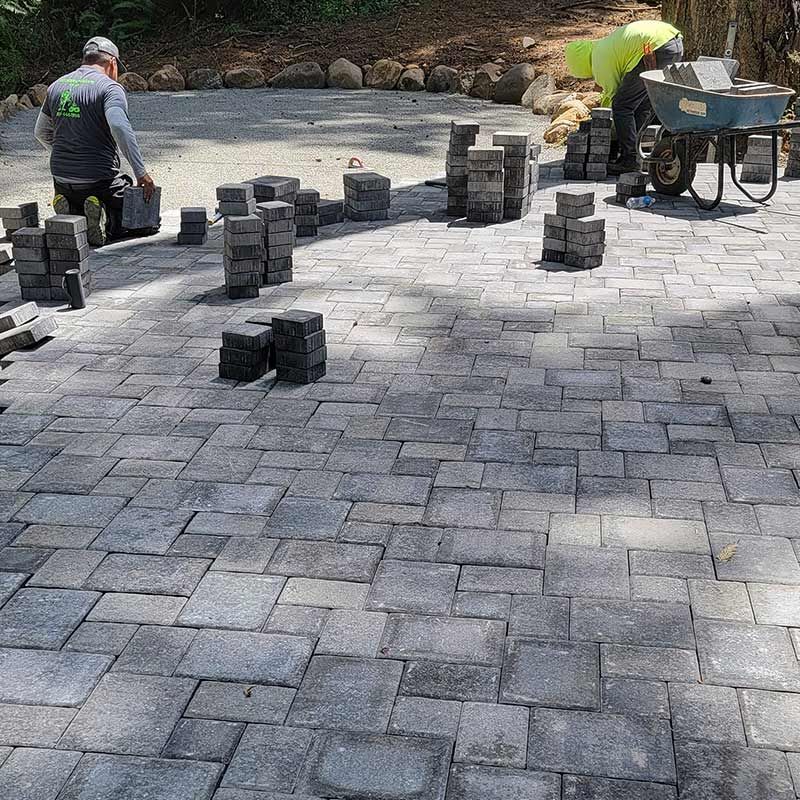 A group of men are working on a brick driveway.