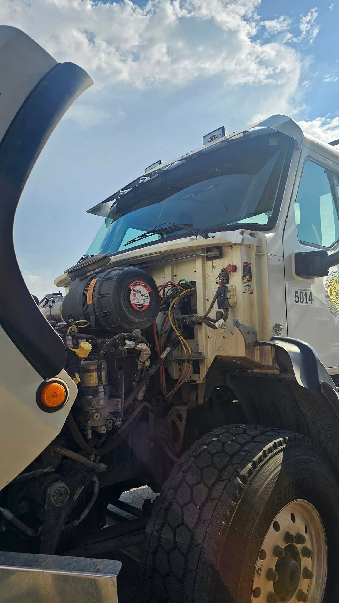 A white truck with its hood up is parked in front of a cloudy sky.