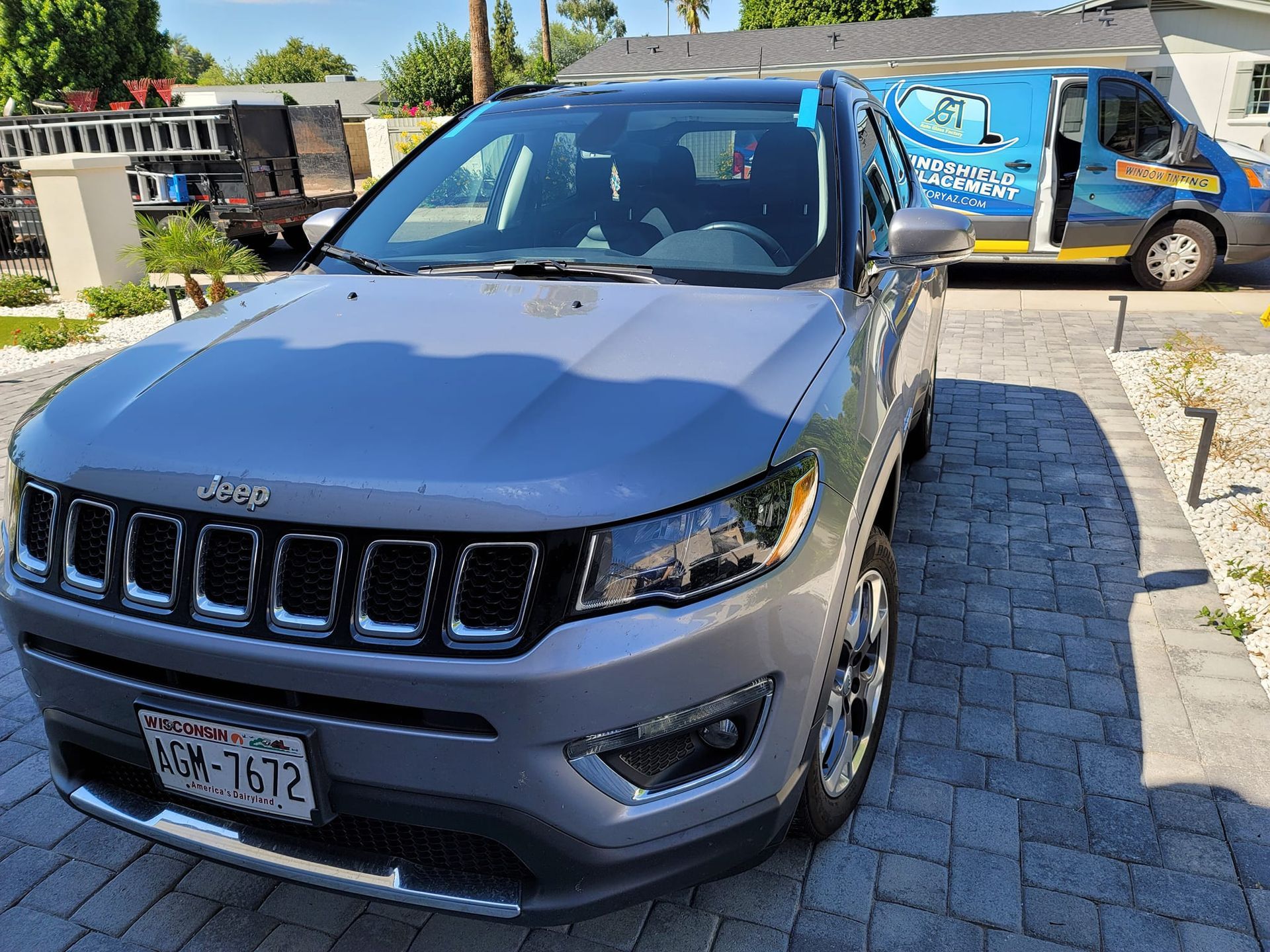 A jeep compass is parked on a brick driveway next to a van.