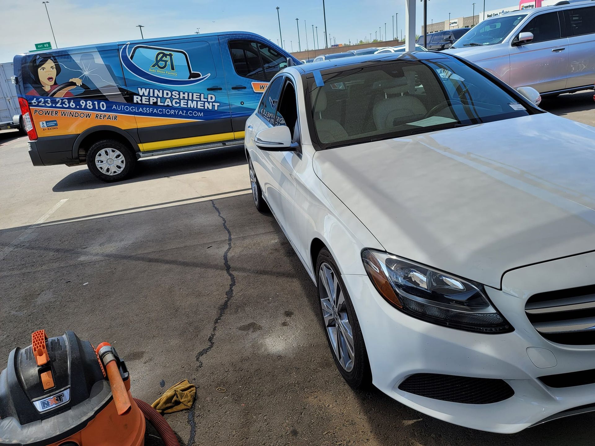 A white car is parked next to a van that says window replacement.