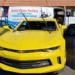 A yellow car is parked in front of an auto glass factory.