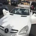 A white mercedes benz slk is parked in a parking lot with its doors open.