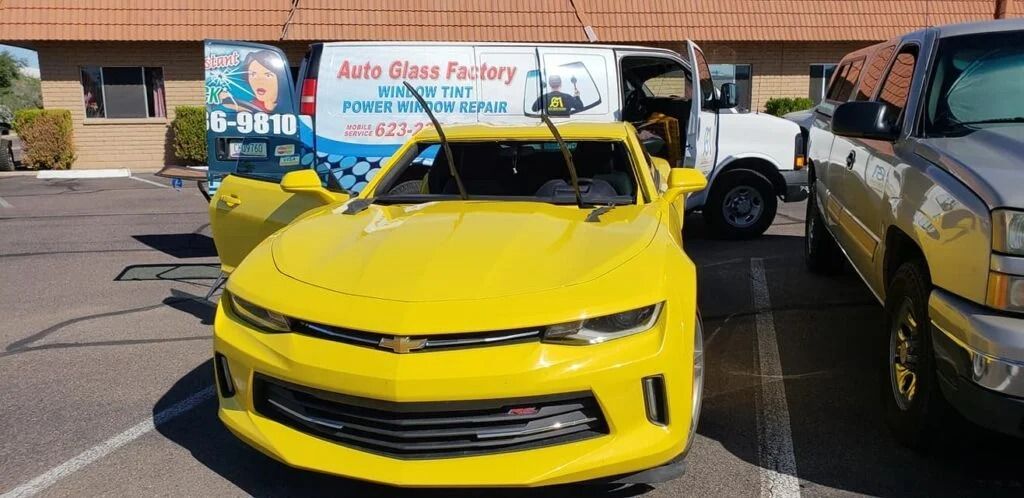 A yellow car is parked in a parking lot next to a truck.