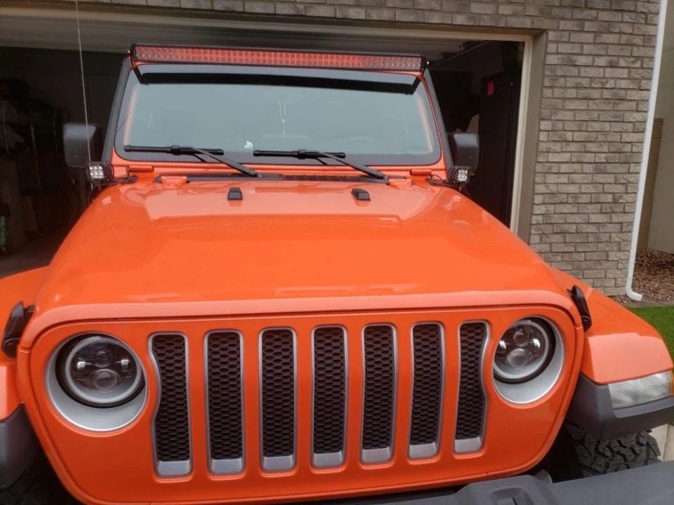 An orange jeep is parked in front of a brick building.
