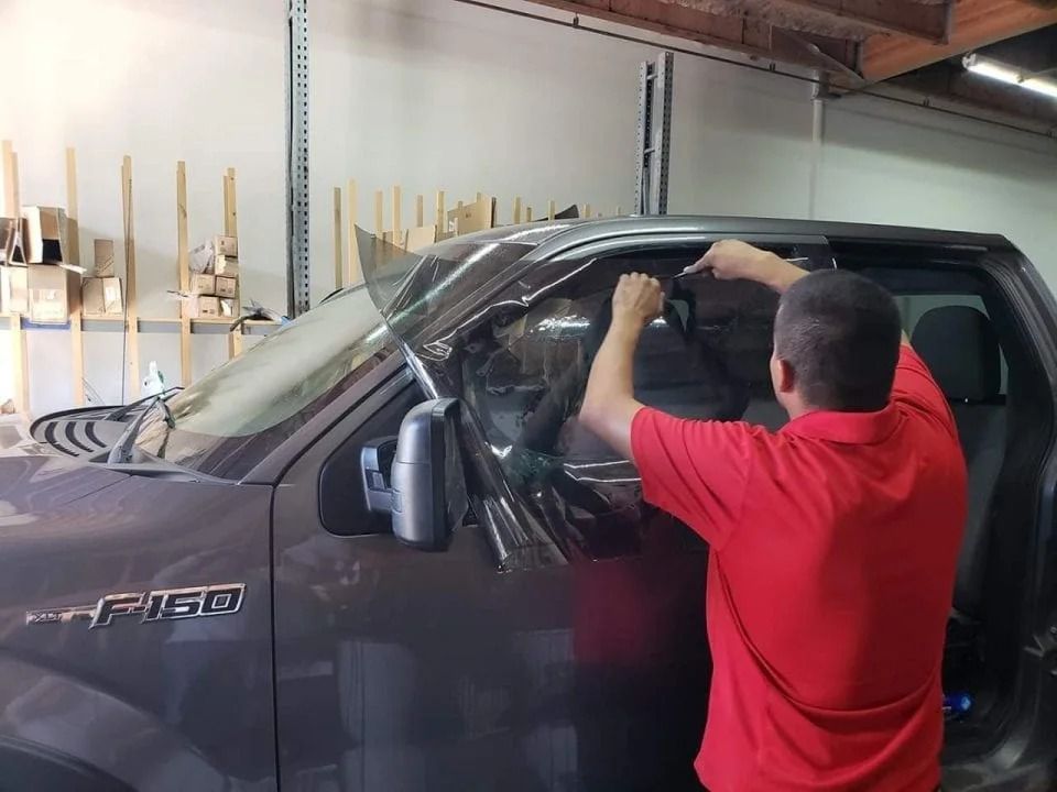 A man in a red shirt is installing window tinting on a truck.