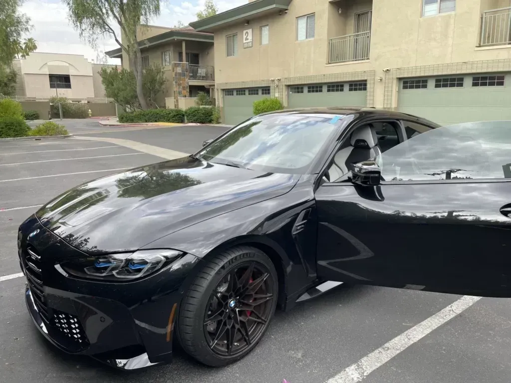 A black car is parked in a parking lot with its doors open.