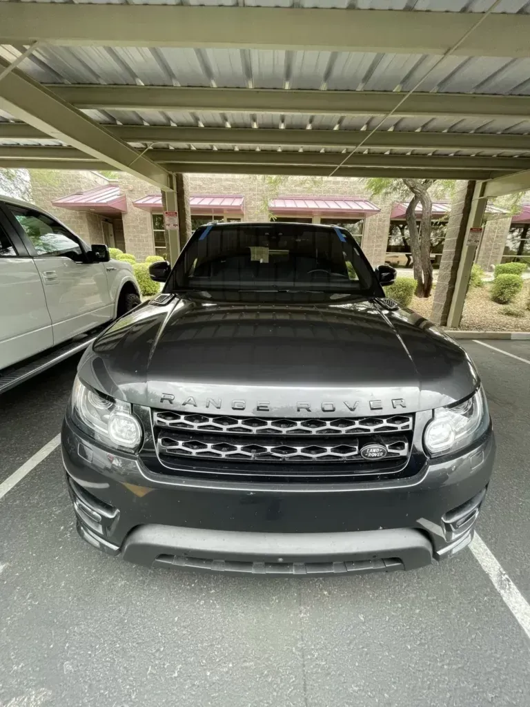 A black range rover is parked under a canopy in a parking lot.