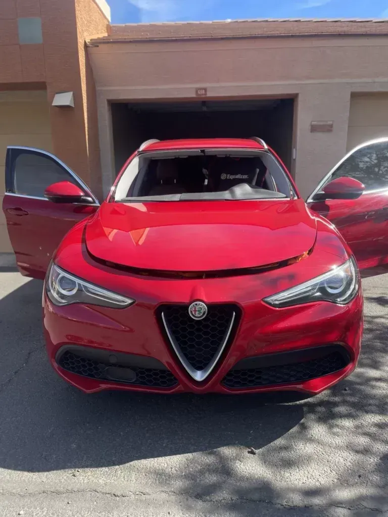 A red car is parked in front of a garage with its doors open.