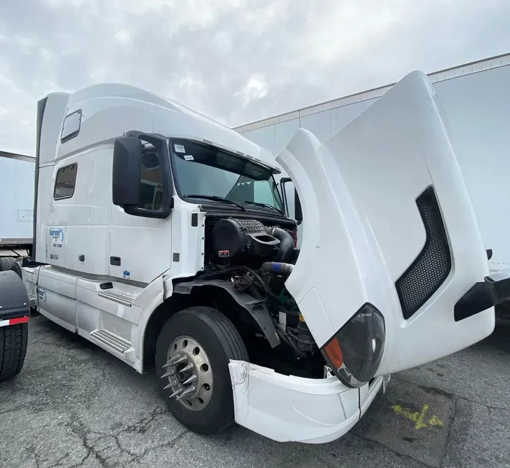 A white semi truck with its hood open is parked in a parking lot.