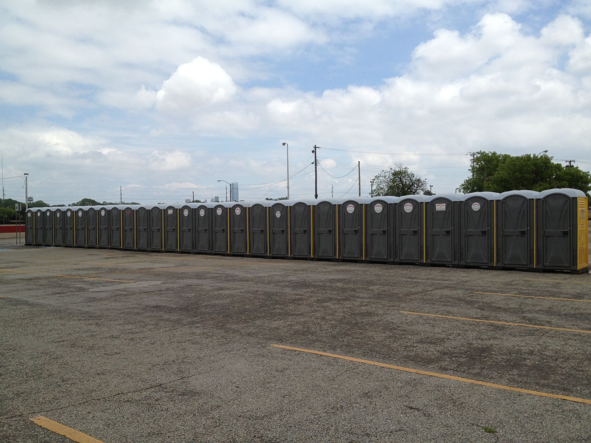 A long line of portable toilets in a gravel parking lot under a cloudy sky.