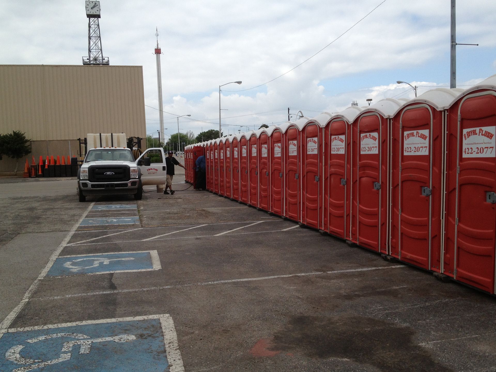 Line of red portable toilets in a parking lot. A man stands near a truck.