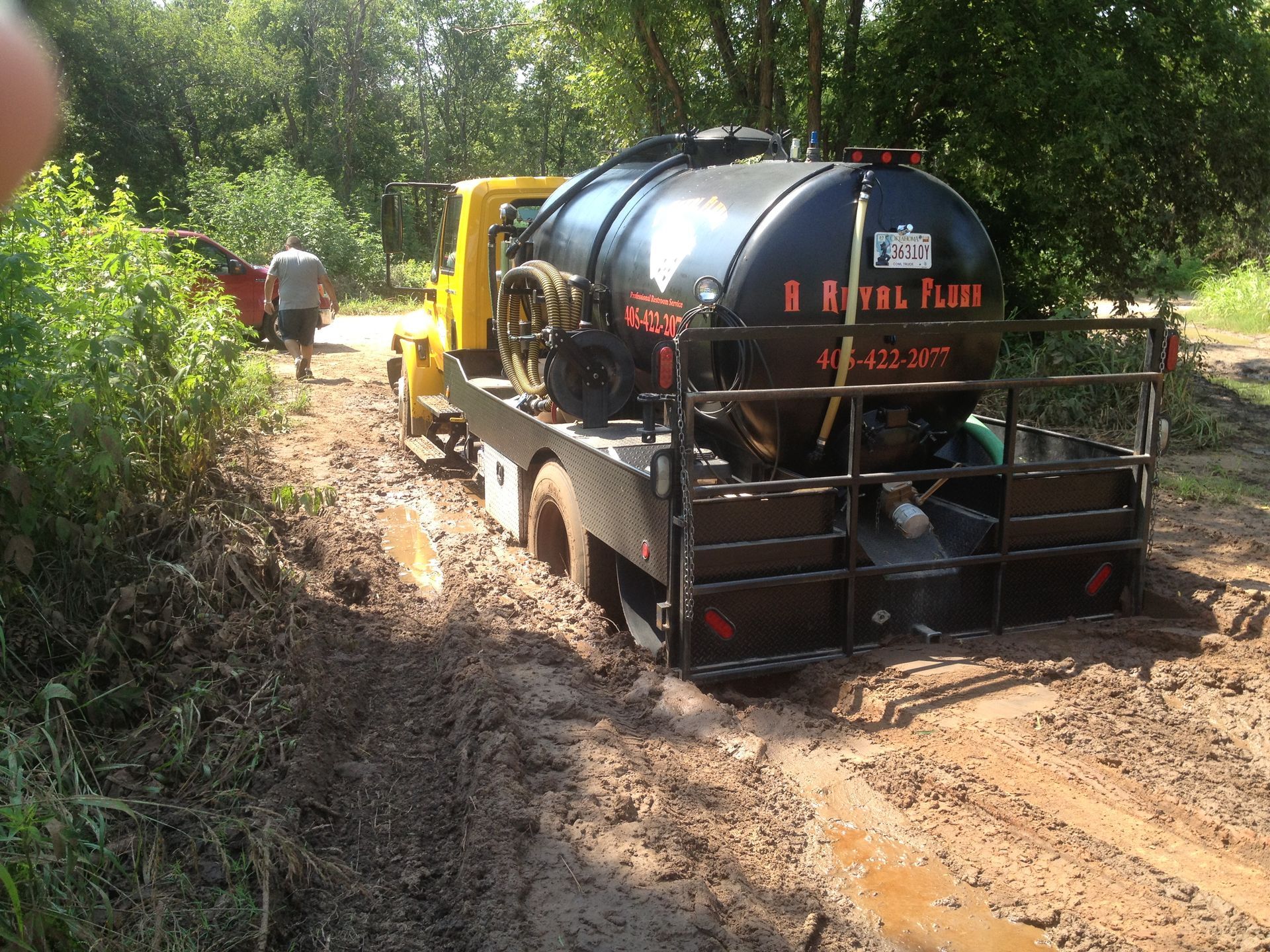 A yellow tanker truck stuck in mud on a dirt road; a person walks toward it.