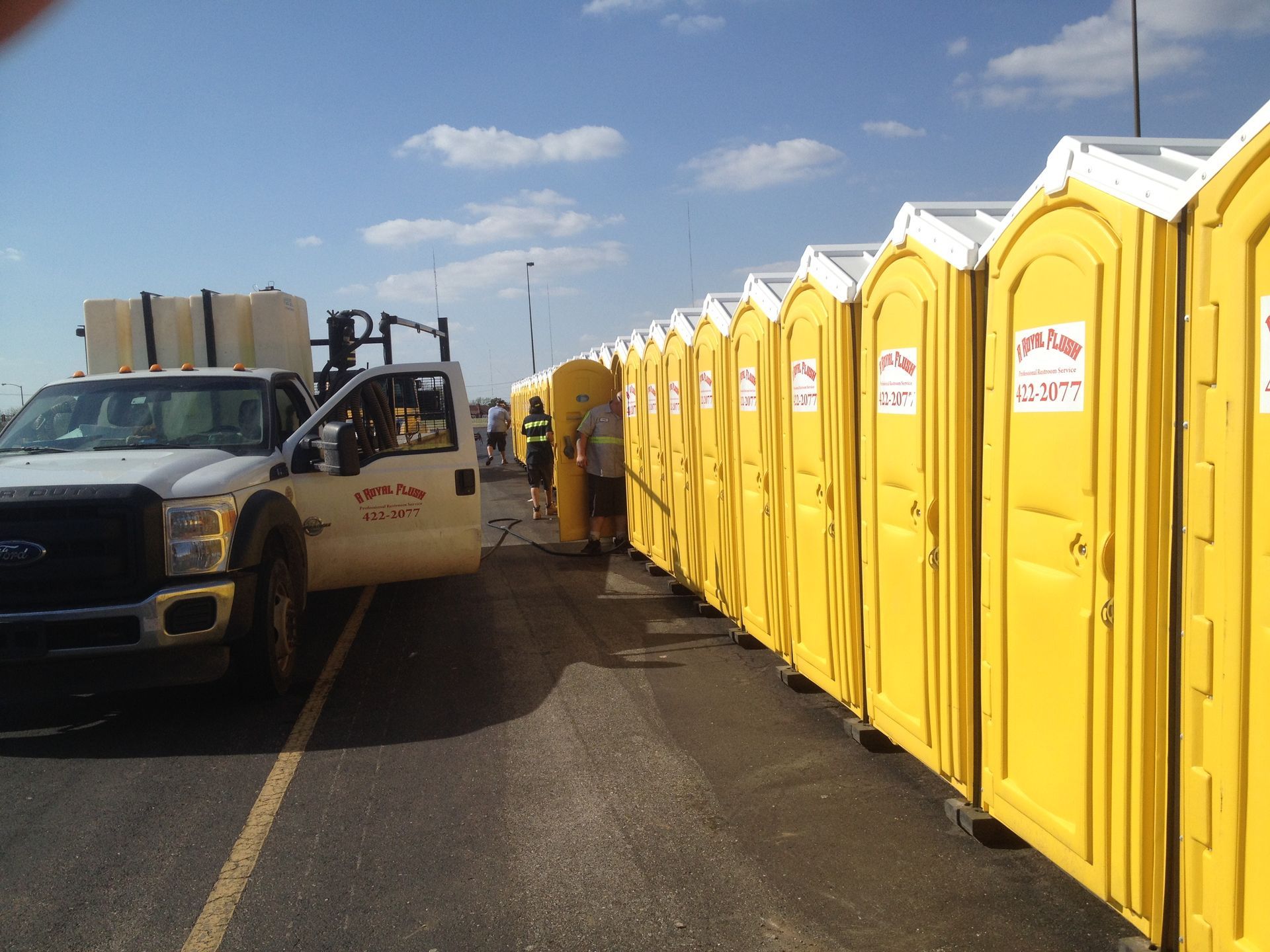 Line of yellow portable toilets with a truck, possibly being serviced, parked alongside.