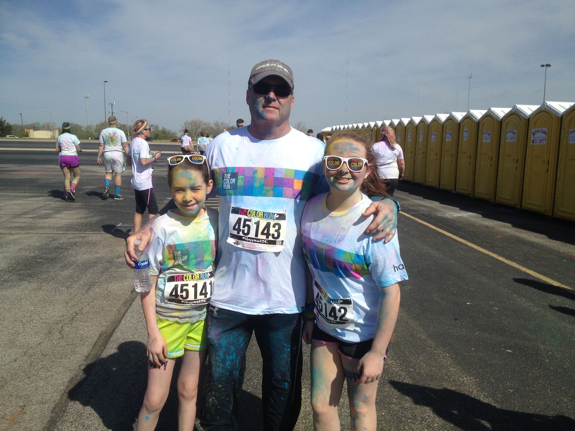 A man and two girls covered in colorful powder pose at an outdoor color run.