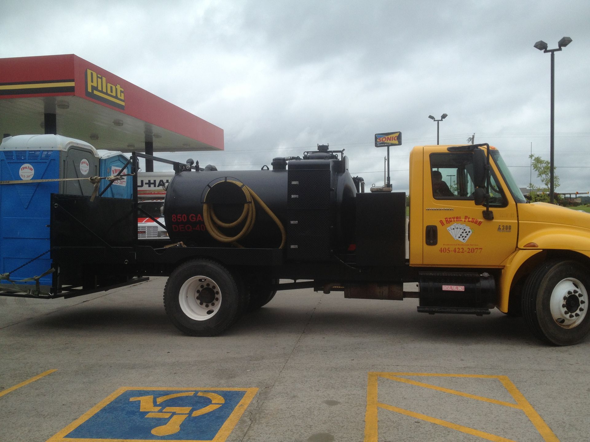 Yellow truck with black tank and portable toilets parked at a gas station.