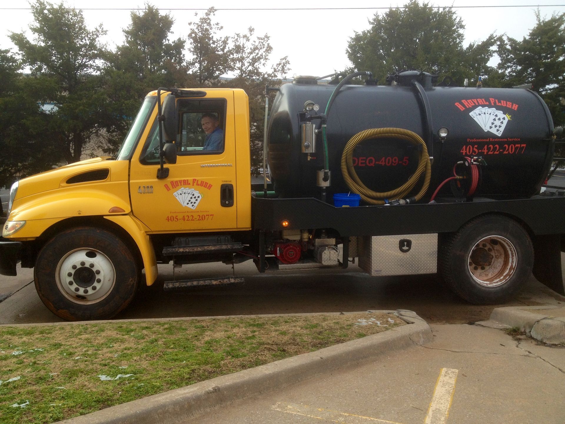 Yellow septic tank truck parked. Driver visible. Black tank with 
